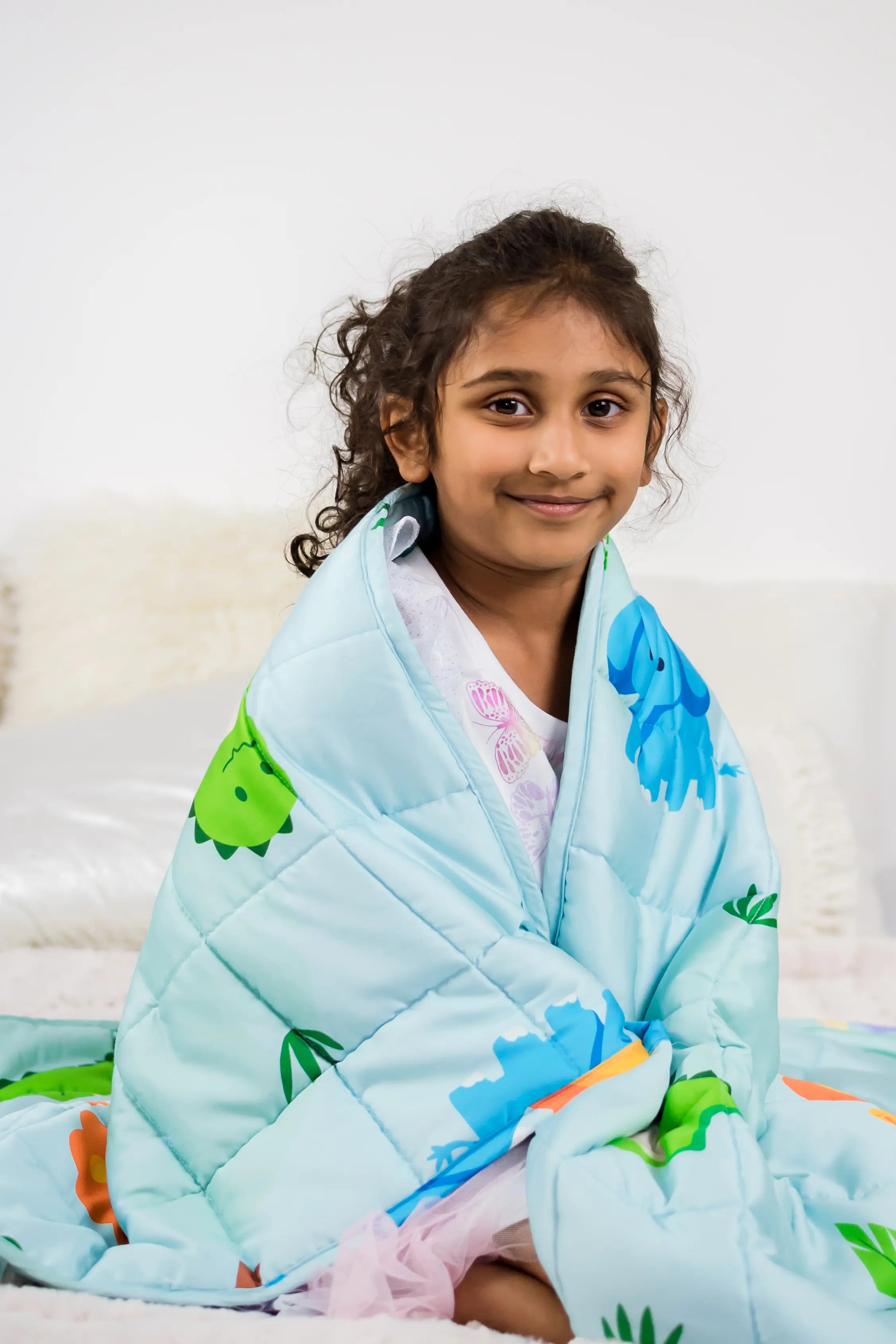 Child wrapped in a dinosaur-themed weighted blanket on a bed